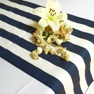 Peut inclure: Un chemin de table rayé blanc et bleu marine avec une fleur blanche et des coquillages sur le dessus.