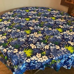 May include: A round blue tablecloth with a tropical floral print featuring white flowers, green leaves, and blue and white flowers.