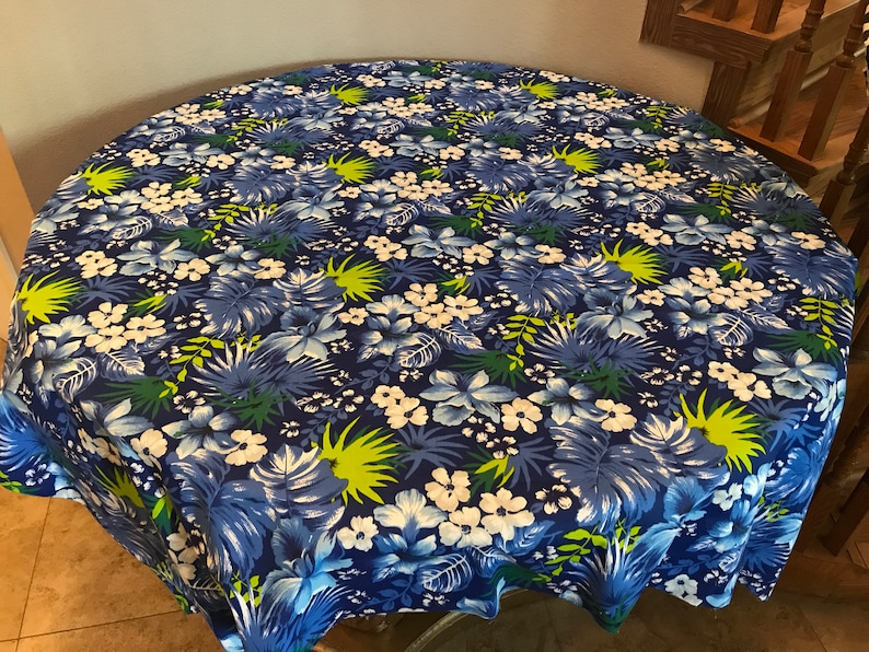May include: A round blue tablecloth with a tropical floral print featuring white flowers, green leaves, and blue and white flowers.