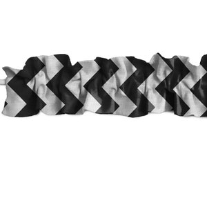 Könnte beinhalten: Ein schwarz-weißes Gardinenvolant mit Chevron-Muster. Der Stoff ist gerafft und hat ein gerüschtes Aussehen. Das Zickzackmuster ist ein klassisches Designelement. Das Volant befindet sich vor einem weißen Hintergrund.