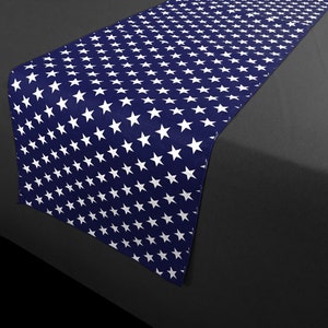 May include: A navy blue table runner featuring a pattern of white stars. The runner is rectangular and appears to be made of fabric. The stars are evenly spaced across the surface, creating a patriotic design.