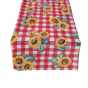 Op de afbeelding: Een rood-wit geruite tafelloper met een patroon van gele zonnebloemen en groene bladeren. De rechthoekige loper, waarschijnlijk van stof, is geschikt voor keuken- of eetkamerdecoratie.