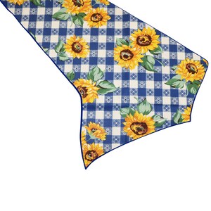 Op de afbeelding: Een decoratieve tafelloper met een blauw-wit ruitpatroon, versierd met gele zonnebloemen en groene bladeren. De loper heeft een donkerblauwe rand en is ontworpen om een vleugje rustieke charme toe te voegen aan elke eettafel.