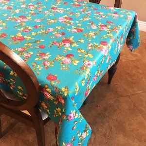 May include: A turquoise tablecloth with a floral pattern featuring pink, red, and white roses. The tablecloth is made of a soft, woven fabric and has a subtle sheen.