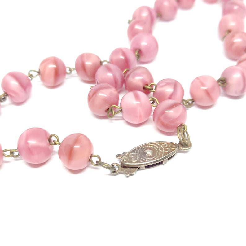 May include: A pink glass bead necklace with a silver clasp. The beads are round and have a swirl pattern.