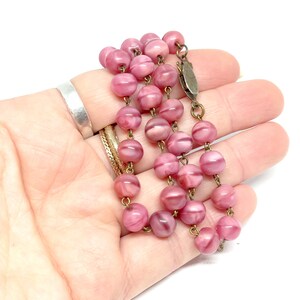 May include: A pink glass bead necklace with a brass clasp. The beads are round and have a swirl pattern.