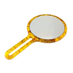 May include: A hand mirror with a round, reflective surface and a handle. The mirror has a yellow and brown tortoiseshell pattern on the frame and handle. The handle has an oval opening for easy grip.
