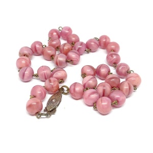 May include: A pink glass bead necklace with a metal clasp. The beads are round and have a swirl pattern.