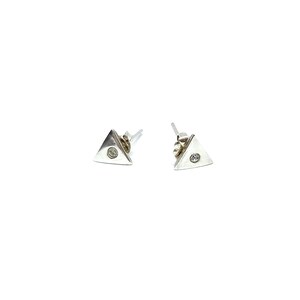 May include: A pair of silver triangle stud earrings. Each earring has a small, clear gemstone set in the centre of the triangle. The earrings are shown against a white background.