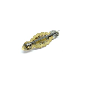 May include: A gold-toned brooch with a detailed floral design and a silver-toned pin. The back of the brooch is marked with the word "Au."
