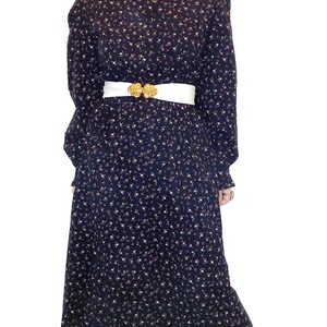 May include: A long-sleeved, black dress with a white floral print and a white belt. The dress has a high neck and a ruffled collar.