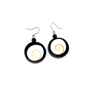 May include: A pair of black and white spiral earrings. Each earring has a black circular frame, a white centre, and a gold spiral design. The earrings have silver hooks and a small black bead.