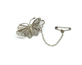 May include: A silver filigree butterfly brooch with a chain and safety pin.