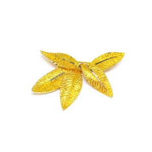 Puede incluir: Broche dorada en forma de hoja con superficie texturizada.