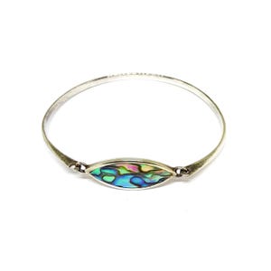 May include: A silver bangle bracelet featuring an oval abalone shell. The shell showcases iridescent colours of blue, green, and pink. The bracelet has a simple, elegant design, suitable for everyday wear.
