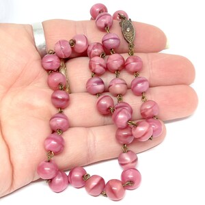 May include: A pink glass bead necklace with a metal clasp. The beads are round and have a swirl pattern.