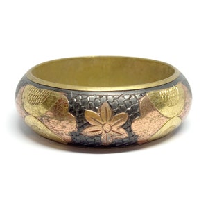 May include: A brass bangle bracelet featuring a black, copper, and gold floral design. The bracelet is wide and has a smooth, polished finish.