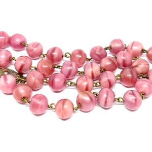 May include: A pink glass bead necklace with a brass chain. The beads are round and have a swirl pattern.