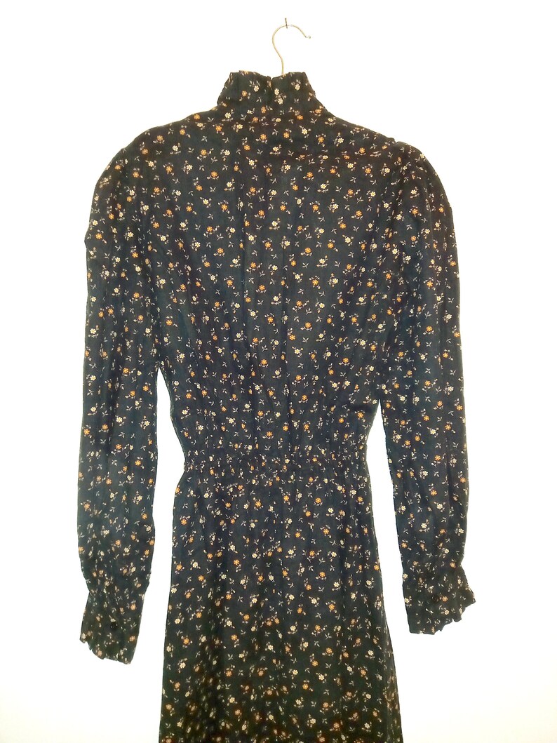 May include: A long-sleeved black dress with a high neck and a floral print. The dress has a fitted bodice and a flowing skirt.