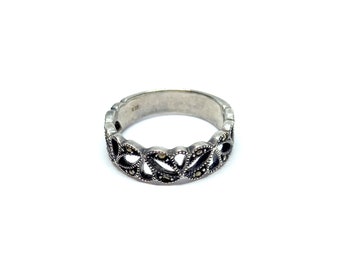 May include: A silver ring with a delicate, intricate design featuring a series of connected marquise-shaped cutouts. The ring is adorned with small, black marcasite stones.