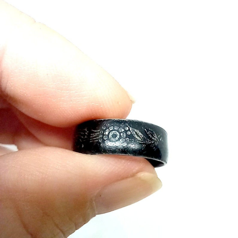 K&ouml;nnte beinhalten: Ein schwarzer Metallring mit einem silbernen Design eines Blumenmusters. Der Ring wird an einem Finger getragen.