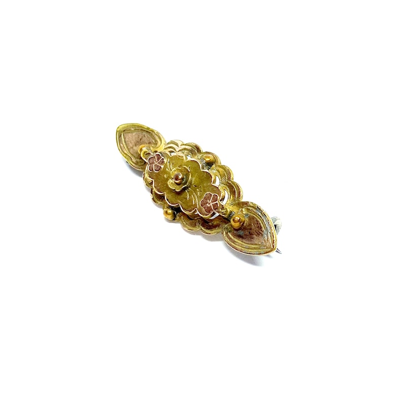 May include: A gold-toned brooch with a floral design and pink accents. The brooch has a pin on the back for attaching to clothing.