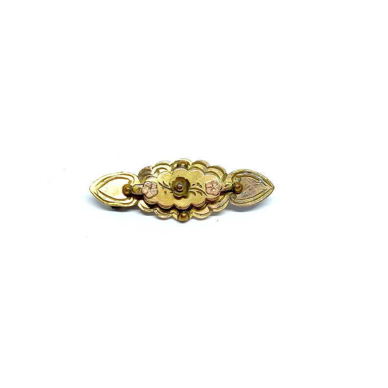 May include: A gold-toned brooch with a floral design and three pink accents. The brooch is shaped like a long oval with a heart-shaped design on each end.