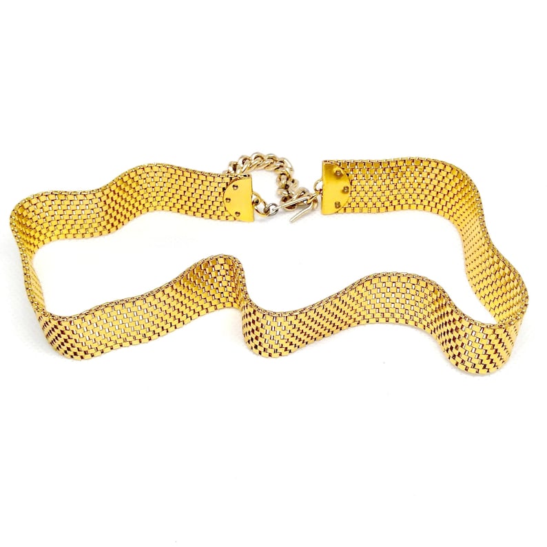 May include: A gold-tone chain belt with a woven mesh design. The belt has a simple clasp closure.
