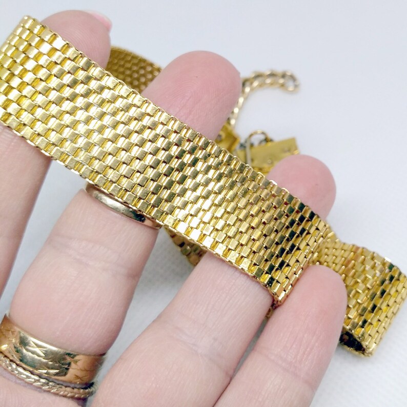 May include: A gold-tone chain bracelet with a woven, mesh design. The bracelet is flexible and has a delicate look.