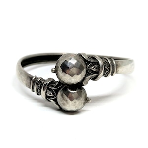 May include: A silver bangle bracelet with two round, textured silver balls and ornate detailing.