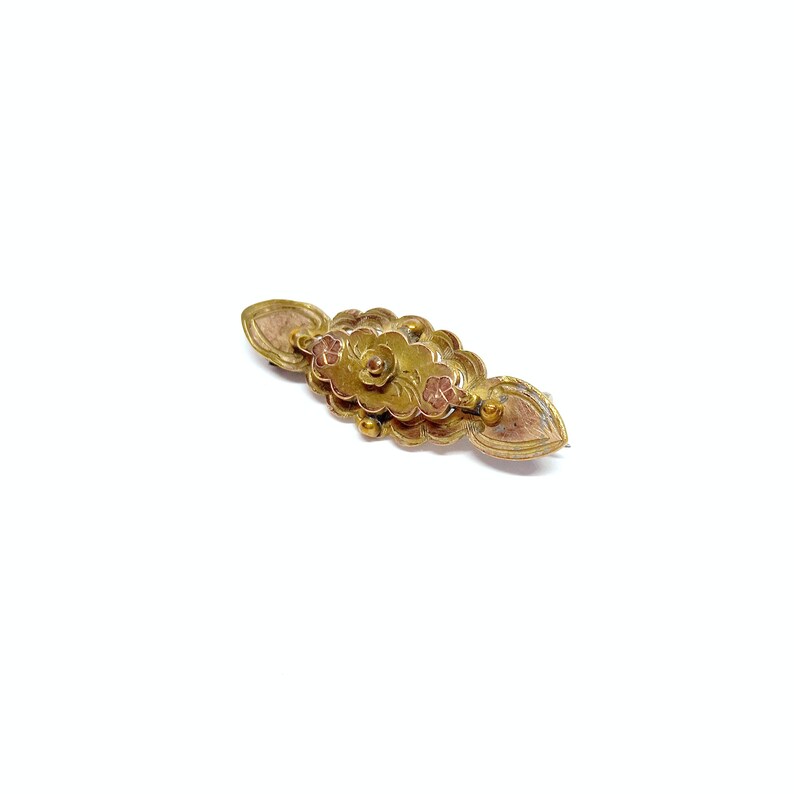 May include: A gold-toned brooch with a floral design. The brooch has a central flower with two smaller flowers on either side. The flowers are raised and have a textured surface.