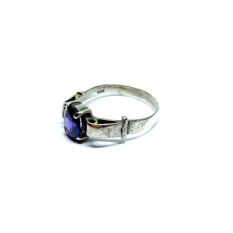 May include: A silver ring with a purple gemstone set in a textured band. The ring is marked "925" on the inside.