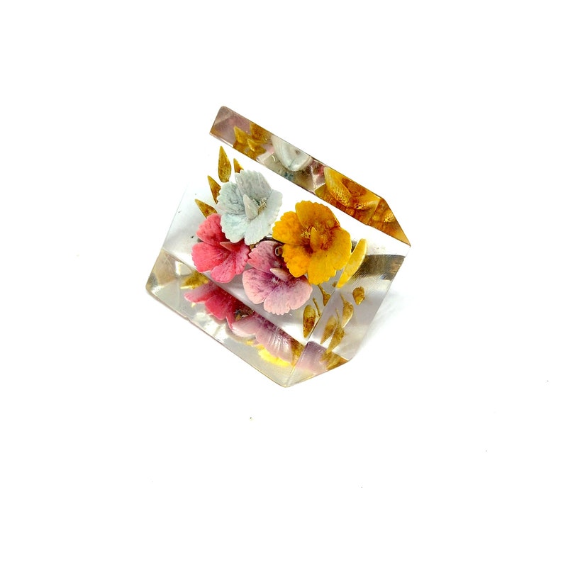 May include: A clear glass paperweight featuring a floral design. The flowers are pink, yellow and blue with gold accents.