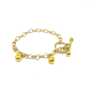 May include: A gold chain bracelet with a toggle clasp and two dangling gold balls.