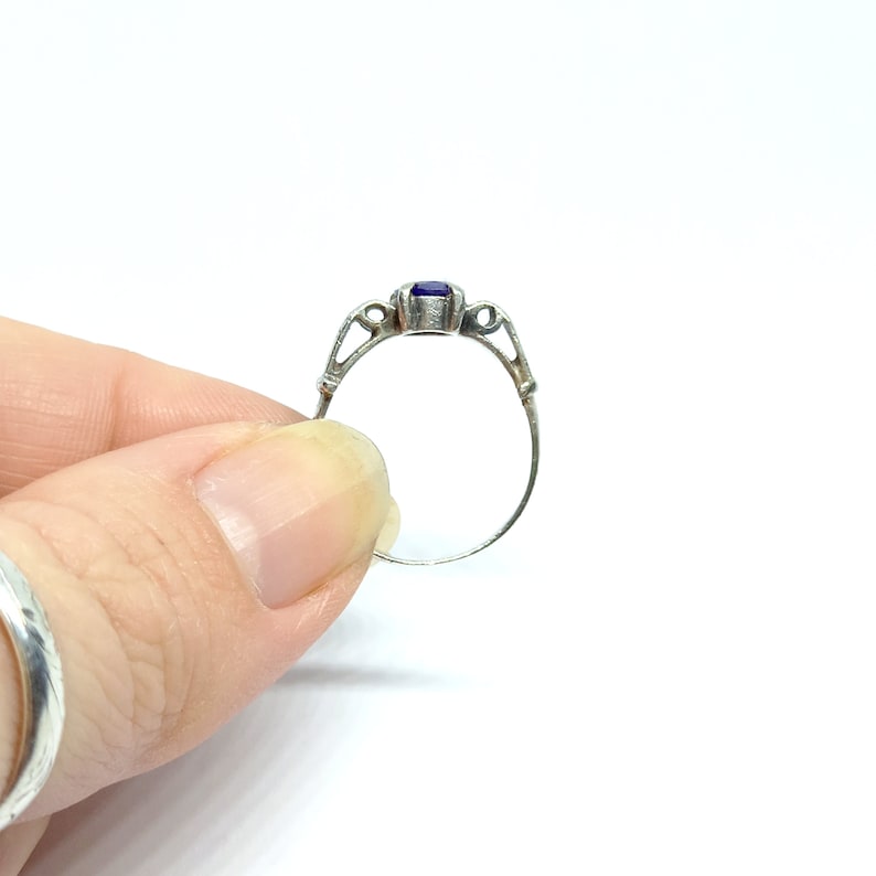 May include: A silver ring with a purple gemstone set in a delicate, ornate design.