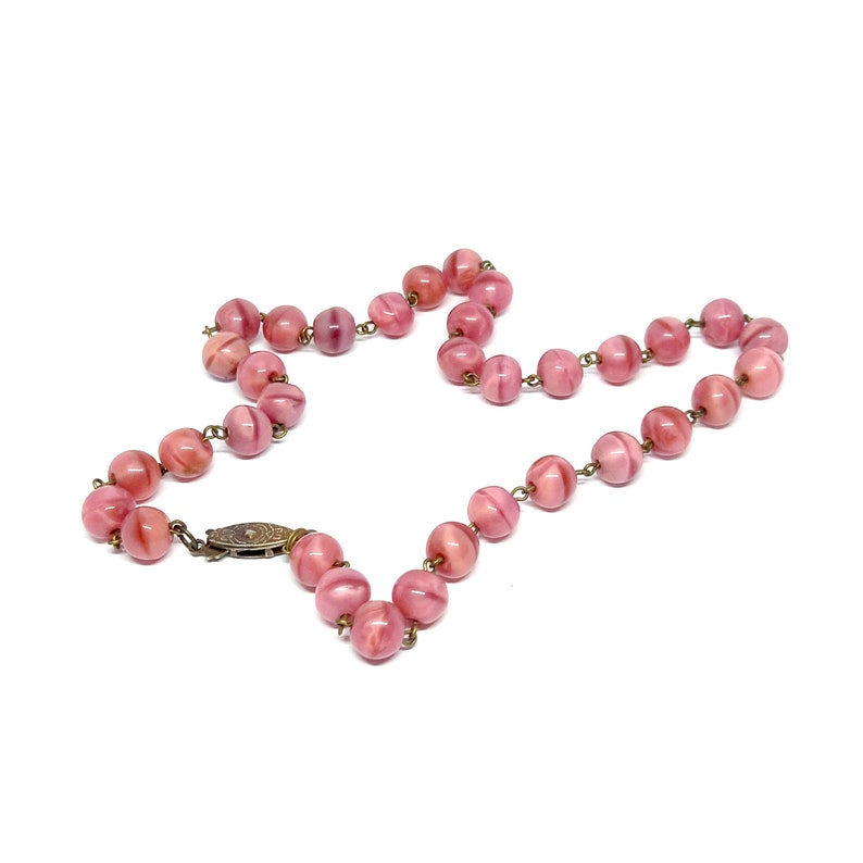 May include: A pink glass bead necklace with a metal clasp. The beads are round and have a swirl pattern.