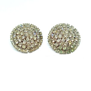 May include: A pair of silver-tone clip-on earrings with a round design. Each earring is covered in clear rhinestones.
