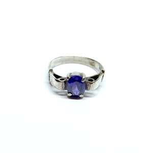 May include: A silver ring with a purple oval-shaped gemstone set in the center.
