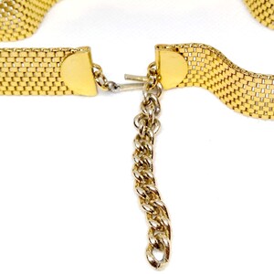 May include: A gold chain belt with a mesh design and a chain extension. The belt is open and the chain extension is hanging down.