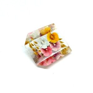 May include: A clear cube paperweight containing a pressed flower arrangement. The flowers are pink, yellow, and white.