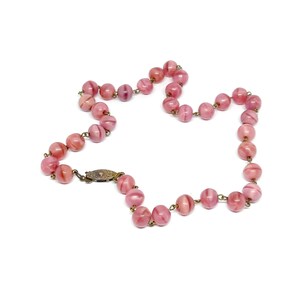 May include: A pink glass bead necklace with a silver clasp. The beads are round and have a swirl pattern.