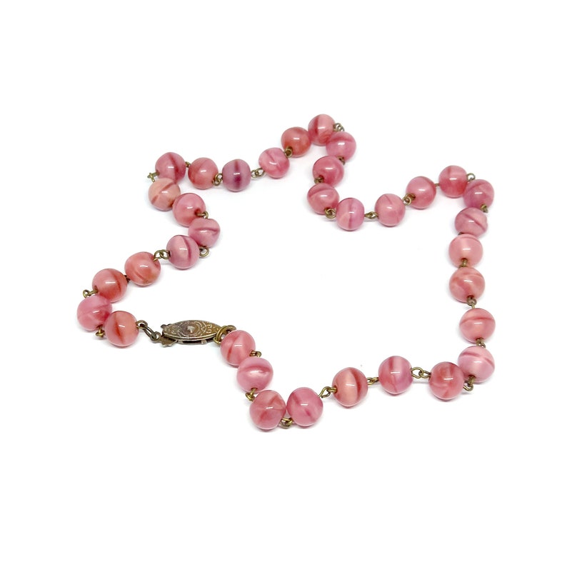 May include: A pink glass bead necklace with a silver clasp. The beads are round and have a swirl pattern.