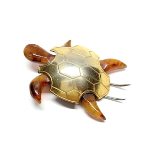 May include: A gold and brown turtle brooch with a detailed shell design. The brooch is made of metal and plastic.