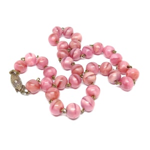 May include: A pink glass bead necklace with a metal clasp. The beads are round and have a swirl pattern.