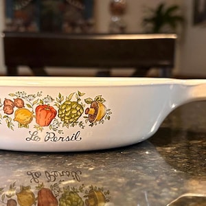 May include: White ceramic skillet with a long handle. The skillet features a colorful illustration of various vegetables and the text "Le Persil". The design includes lemons, a red bell pepper, and artichokes.