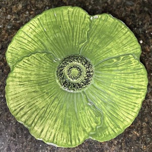 May include: A green ceramic decorative plate in the shape of a flower. The plate has a textured surface with a detailed center and petal design. The plate is a bright, spring green color.