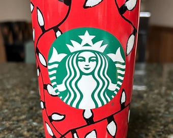May include: A red Starbucks travel tumbler featuring a repeating pattern of black-outlined white holiday light bulbs connected by black lines. The iconic green and white Starbucks siren logo is centered on the front of the cup.