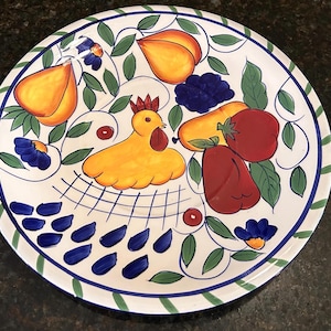 May include: White ceramic decorative plate with a hand-painted design featuring a yellow chicken, various fruits, and blue and green accents. The plate has a blue and green border.