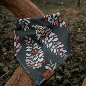May include: Dark teal dog bandana with a colorful abstract pattern of white, pink, orange, and yellow shapes. The bandana is square-shaped and has a brown leather tag that says "RISING RIVER".