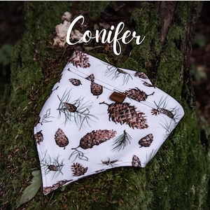 May include: White bandana with a brown pine cone pattern. The bandana has the word "Conifer" printed on it.
